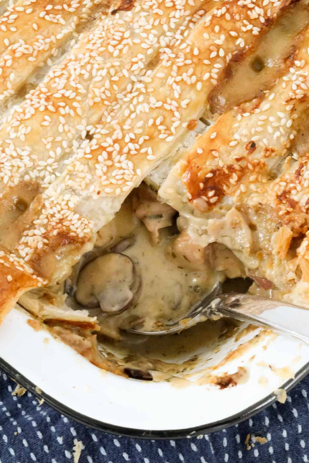 A baking dish filled with a creamy chicken and mushroom filing and topped with strips of golden puff pastry.