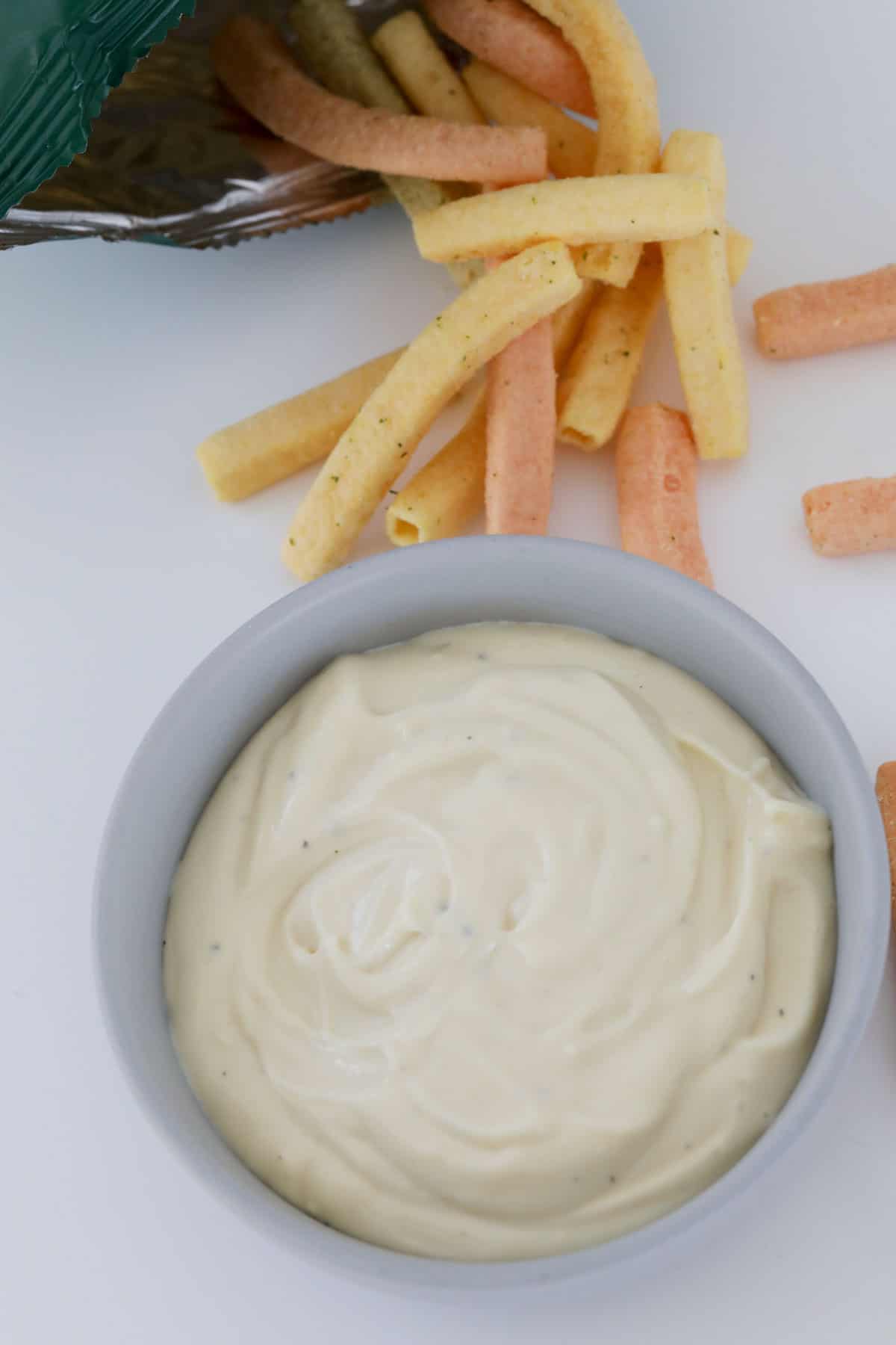 An overhead shot of a bowl filled with aioli with vegetable chips nearby.