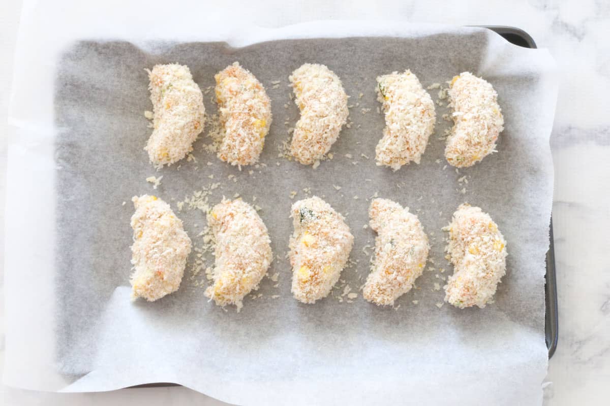Uncooked nuggets coated in panko crumbs on a paper lined oven tray.