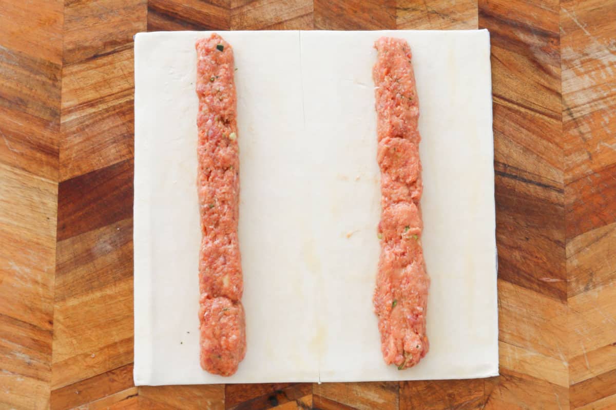 A sheet of puff pastry cur into two, with a line of sausage mince filling down the centre of each pastry rectangle.