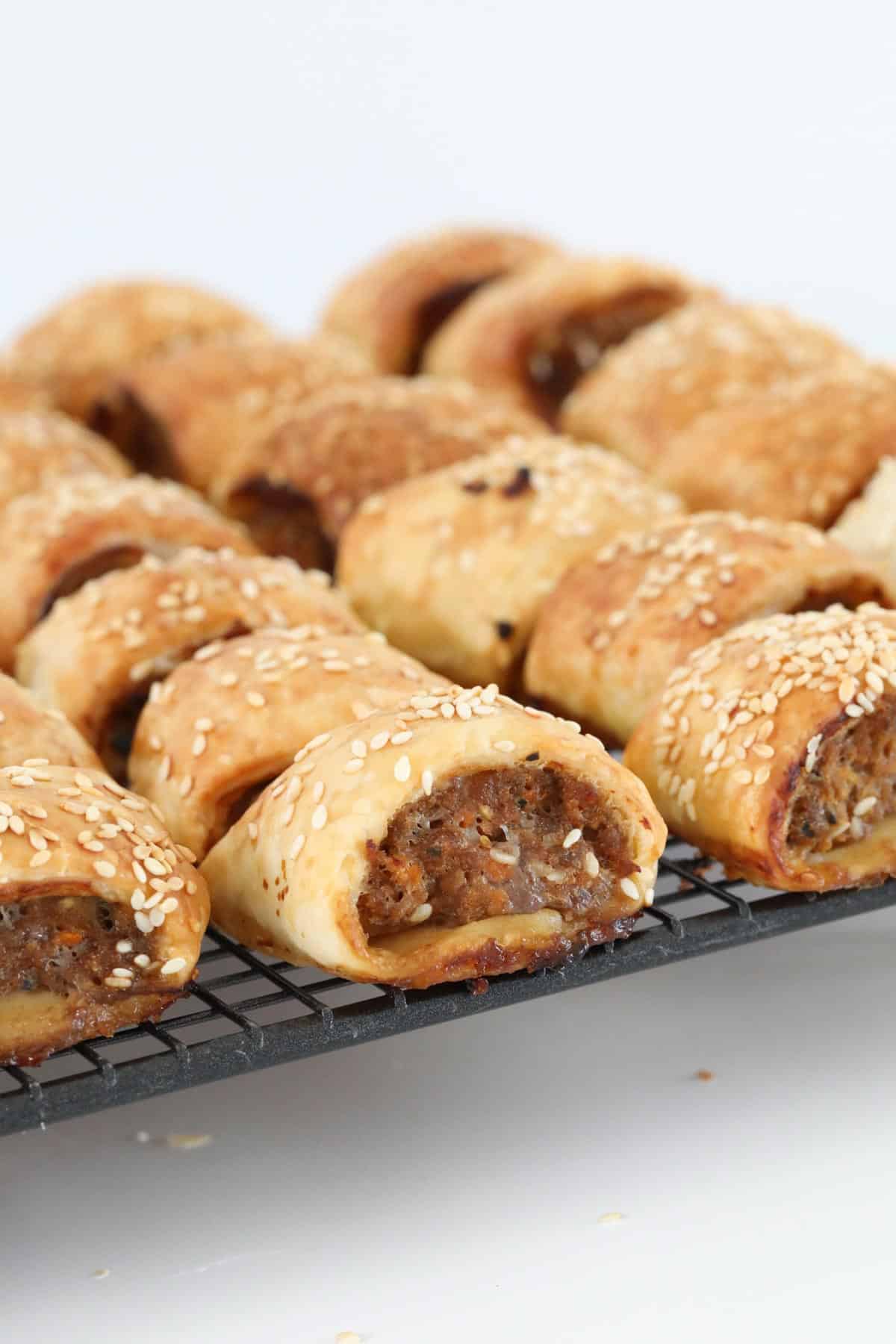 Golden baked beef sausage rolls sprinkled with sesame seeds on a wire rack