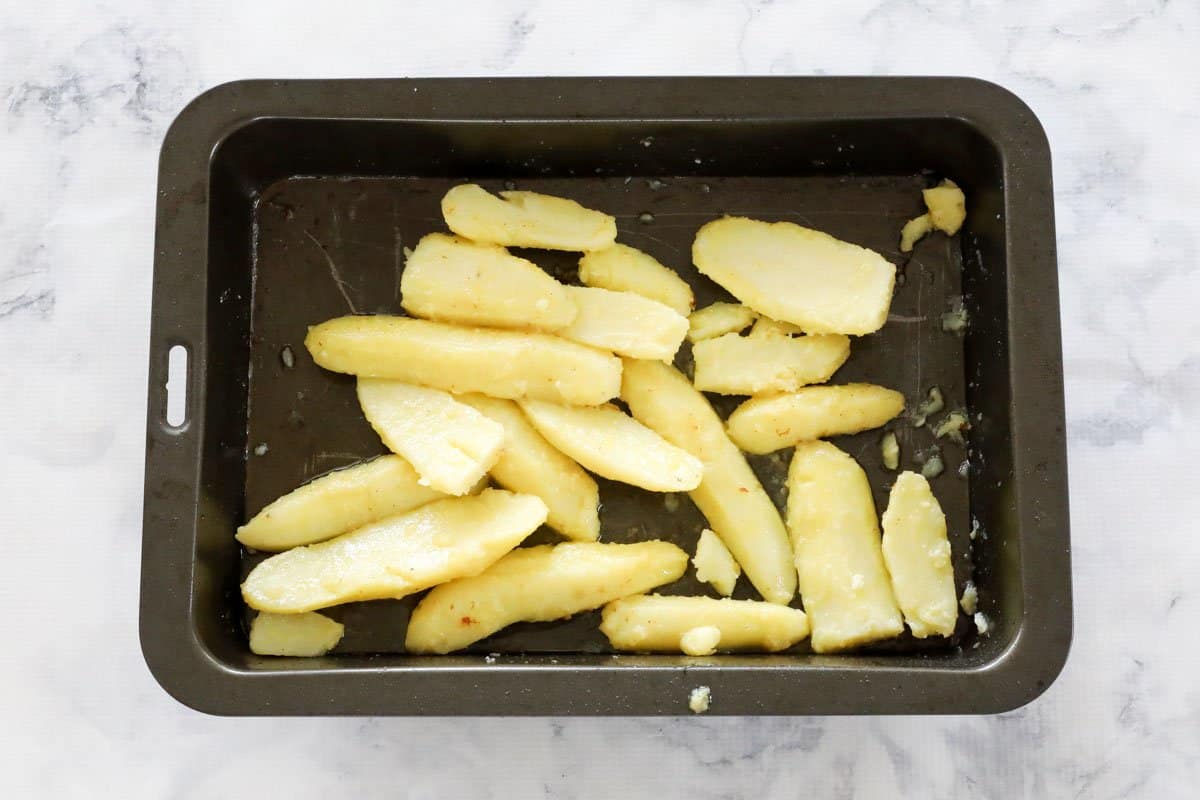 Par cooked wedges in a tray coated with oil and butter.