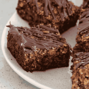 Pieces of oat and date slice on a plate with a drizzle of chocolate on top.