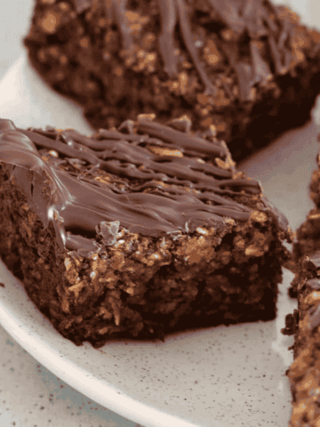 Pieces of oat and date slice on a plate with a drizzle of chocolate on top.