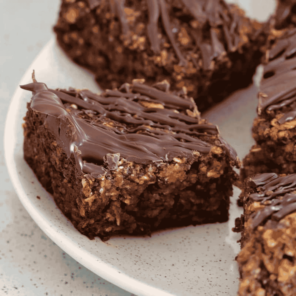 Pieces of oat and date slice on a plate with a drizzle of chocolate on top.