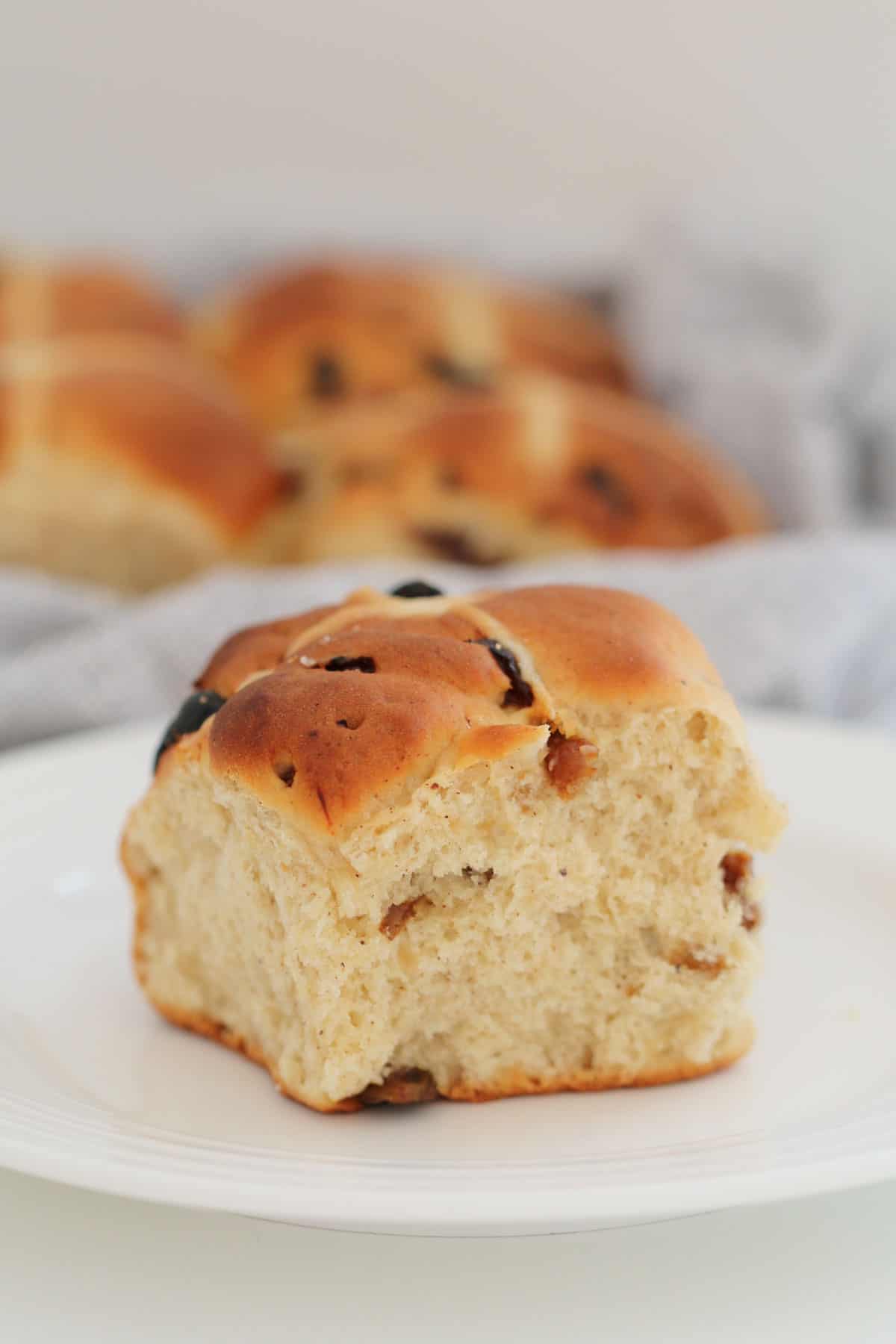A fluffy fruit hot cross bun spied with cinnamon and nutmeg on a white plate.