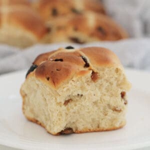 A fluffy fruit hot cross bun spied with cinnamon and nutmeg on a white plate.