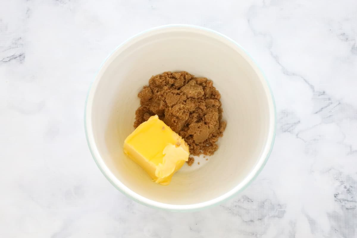 A white bowl with brown sugar and a cube of softened butter on a marble counter