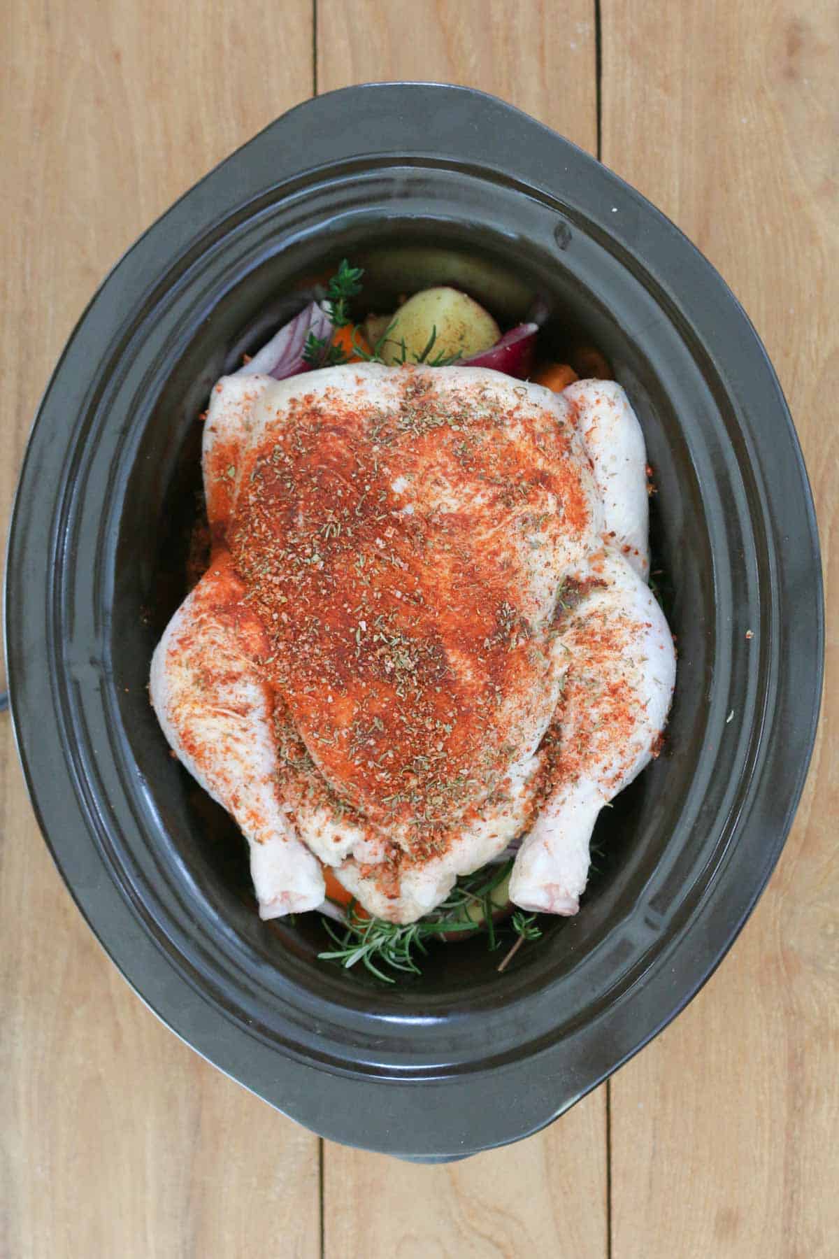 A seasoned uncooked chicken in a crock pot.