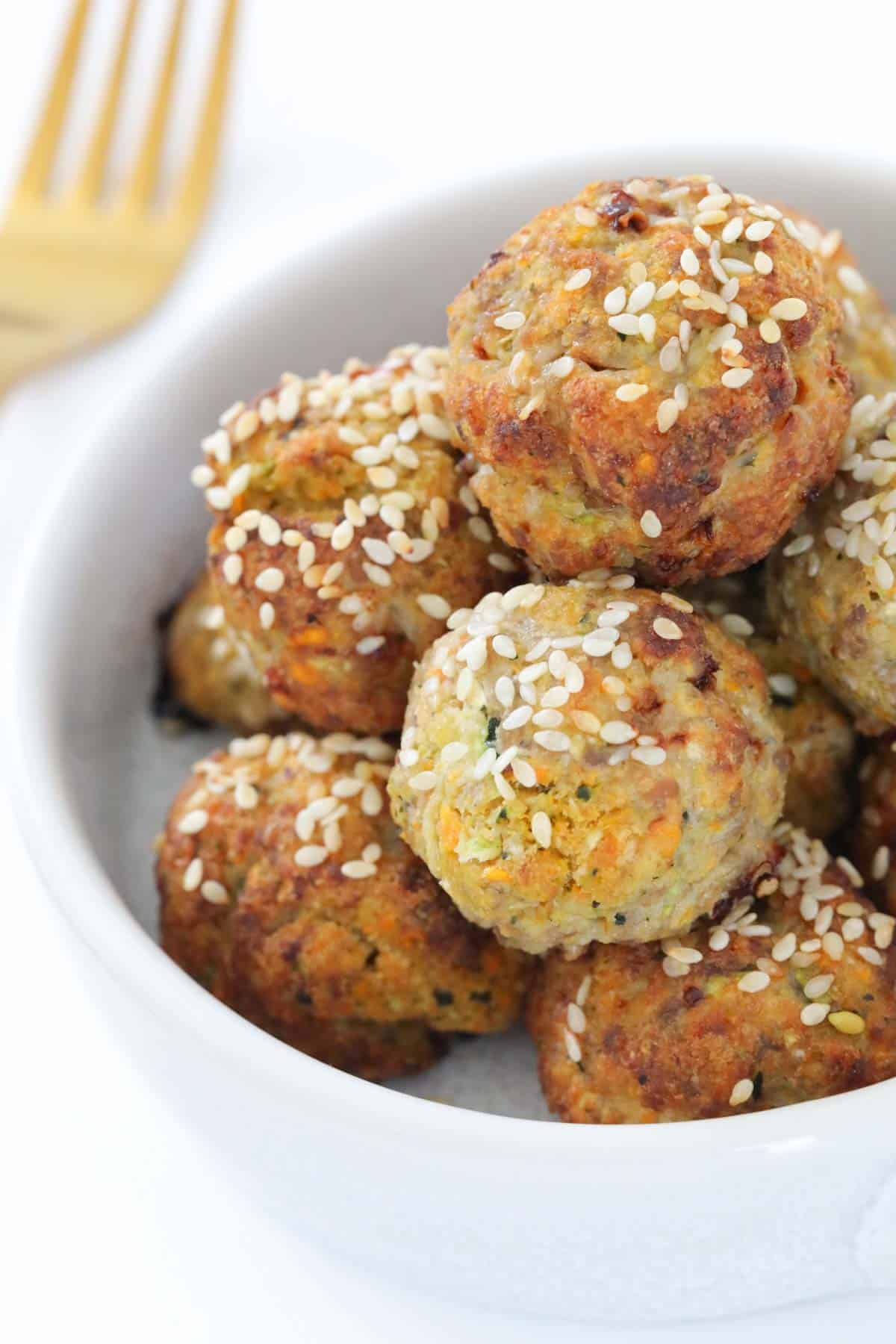 A close up of sesame seeds sprinkled over baked meatballs in a white bowl