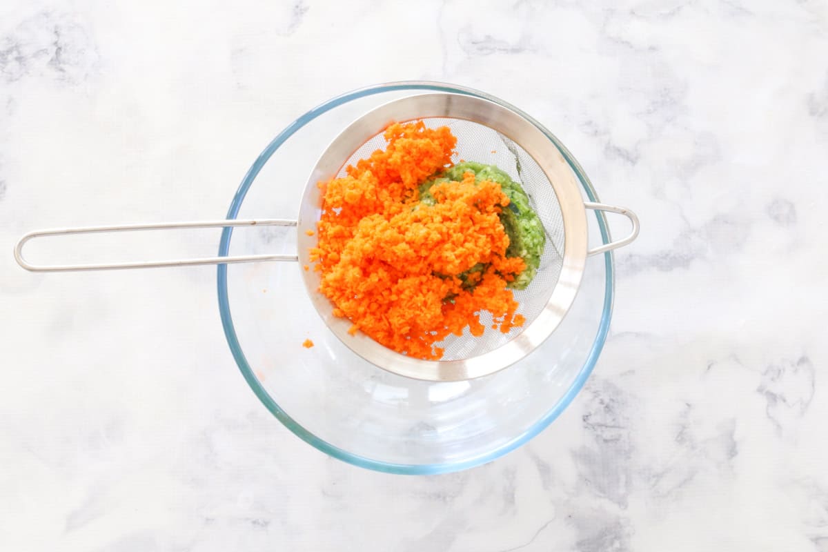Finely grated carrot and zucchini in a wire strainer over a glass bowl