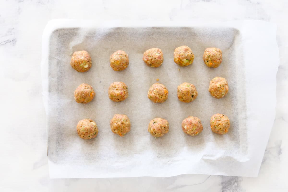 Fifteen meatballs spaced on baking paper on a tray