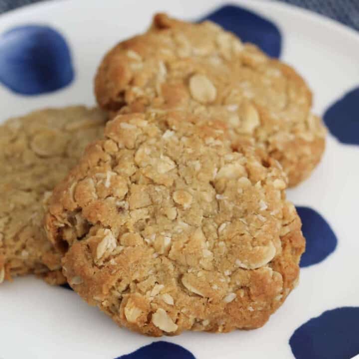 A blue and white spotted plate with three ANZAC biscuits on top.