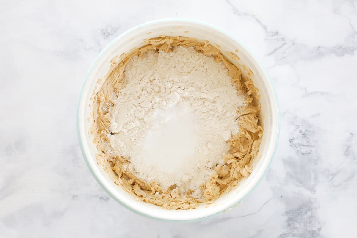 Flour on top of cookie dough in a bowl.