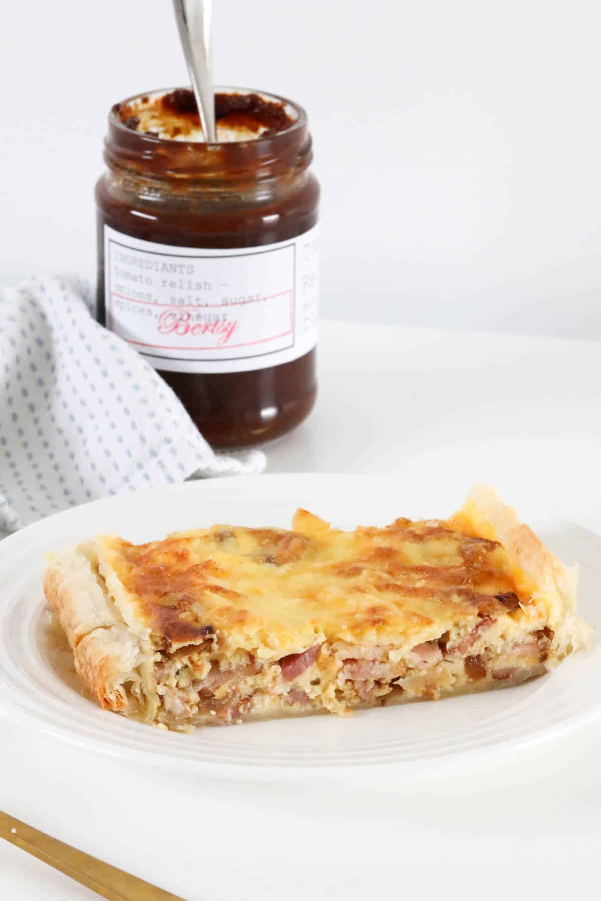 Egg and bacon pie on a white plate with a jar of tomato relish in the background.