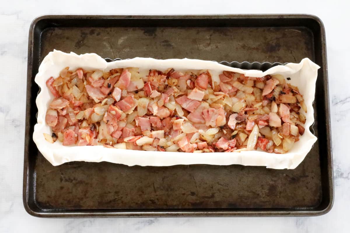 Bacon and onion layered over puff pastry base in baking tin.