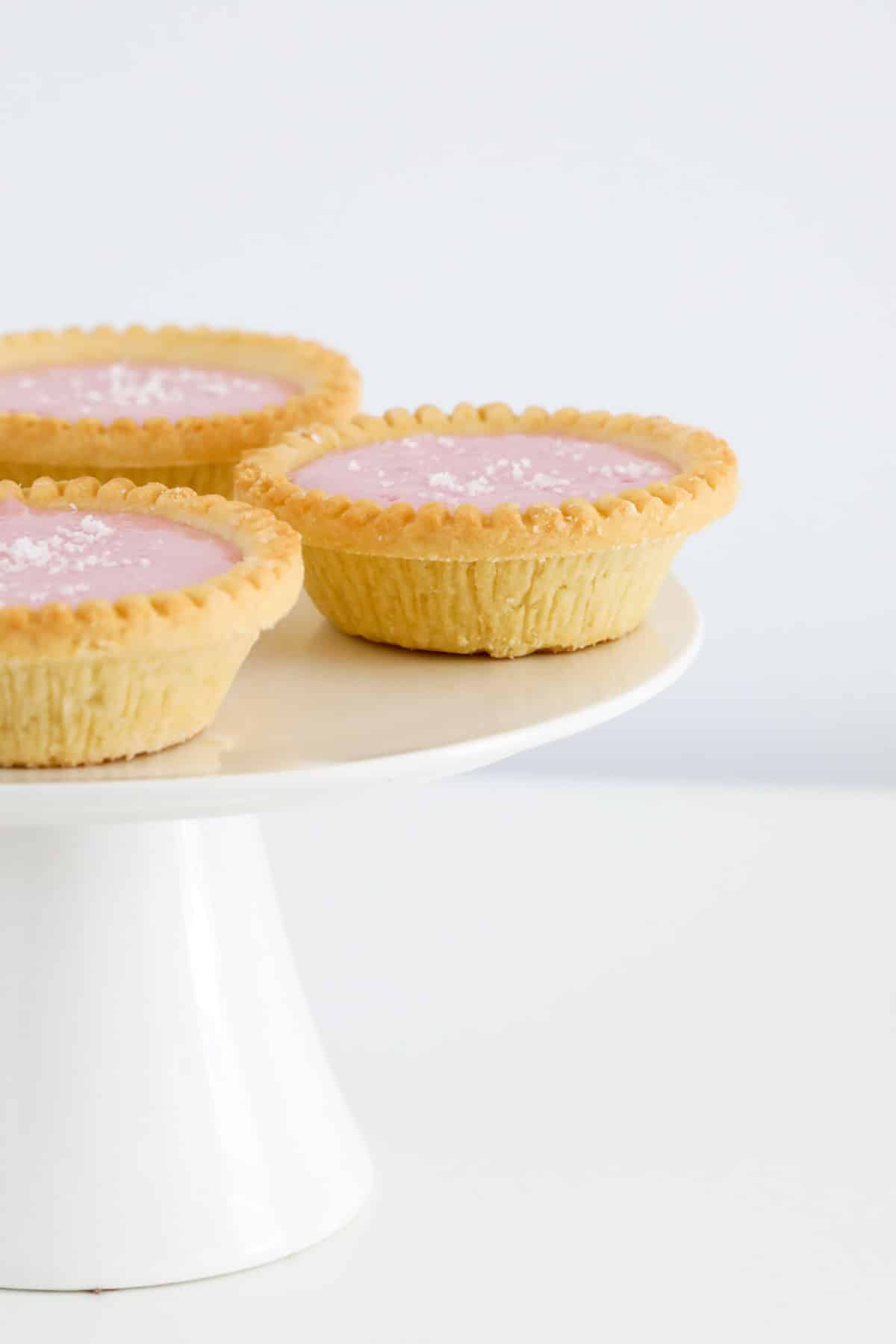 Mini pastry shells filled with pink marshmallow filling on a cake stand.