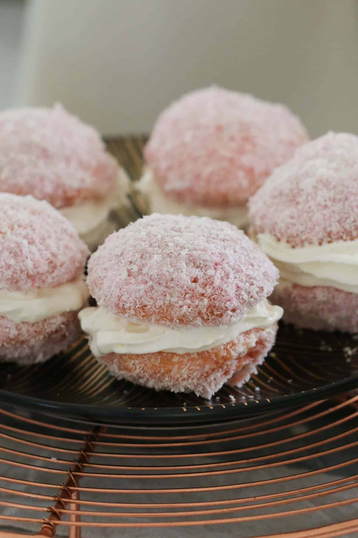 Coconut, jelly and cream sandwich cakes on a wire rack.