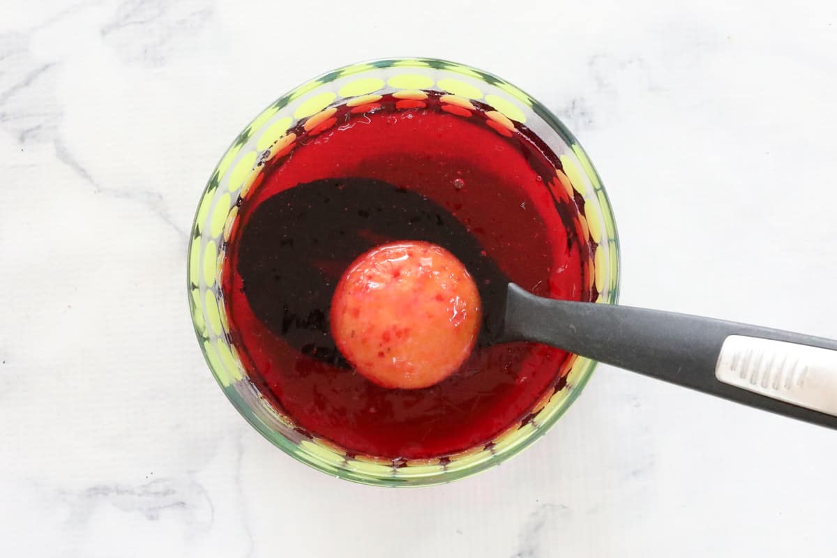 A spoon holding a small sponge cake in a bowl of raspberry jelly.