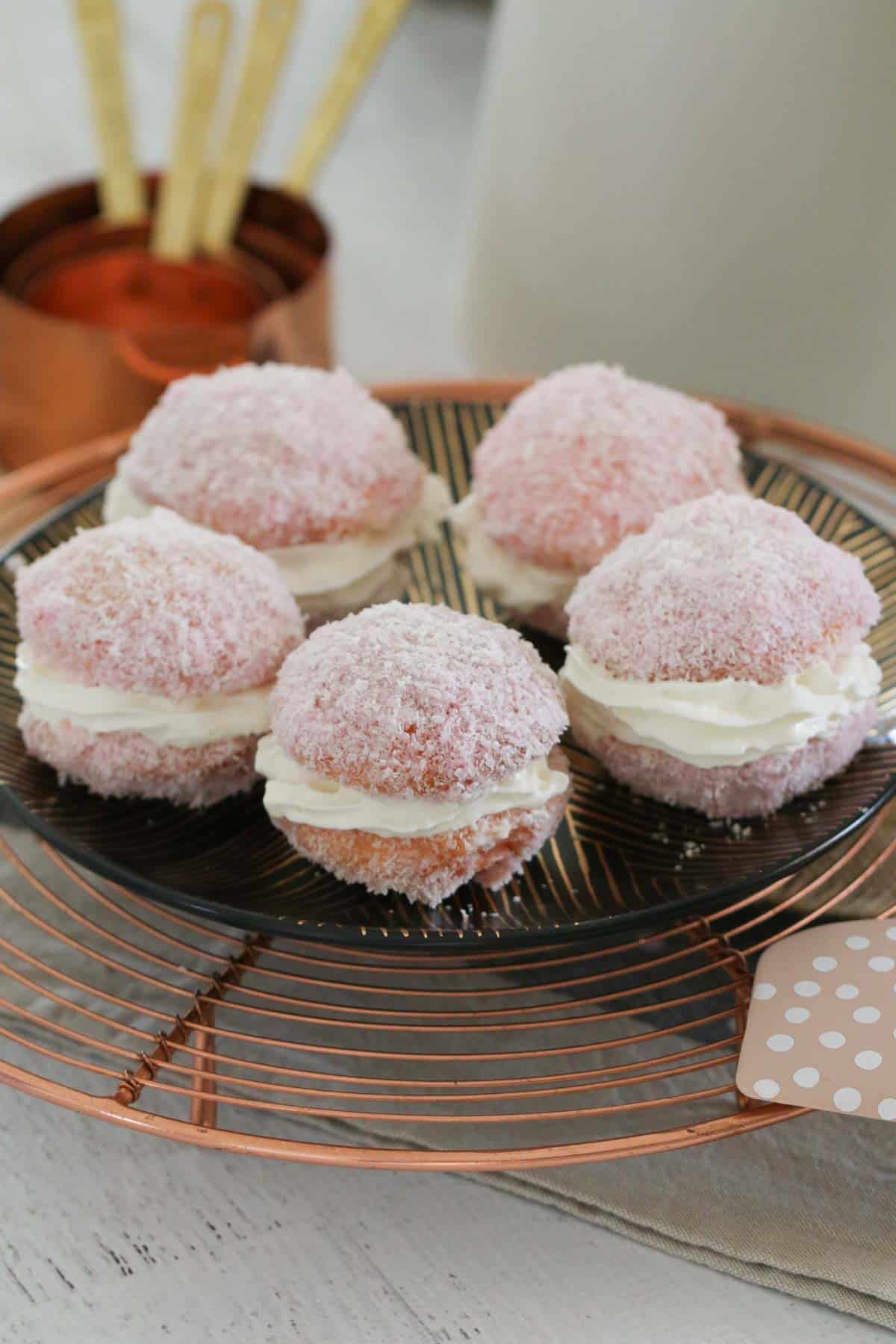 Five jelly cakes filled with whipped cream and served on a black plate.