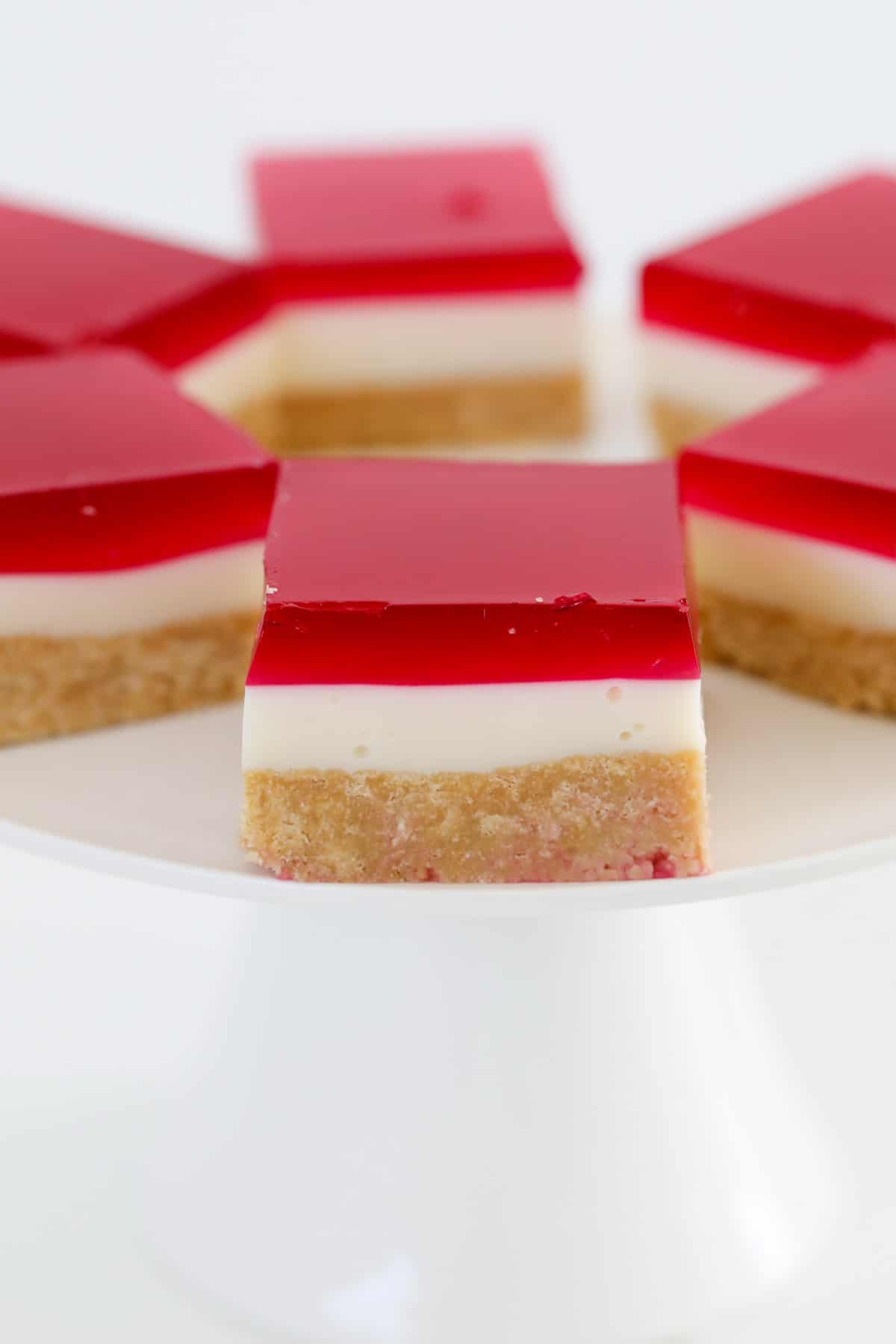Pieces of slice topped with raspberry jelly on a white cake stand.