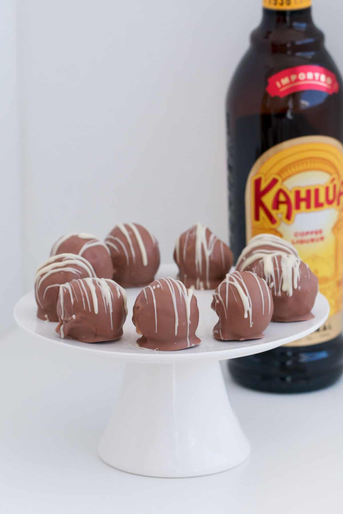 Kahlua cheesecake balls on a white cake plate in foreground with bottle of kahlua bottle in background
