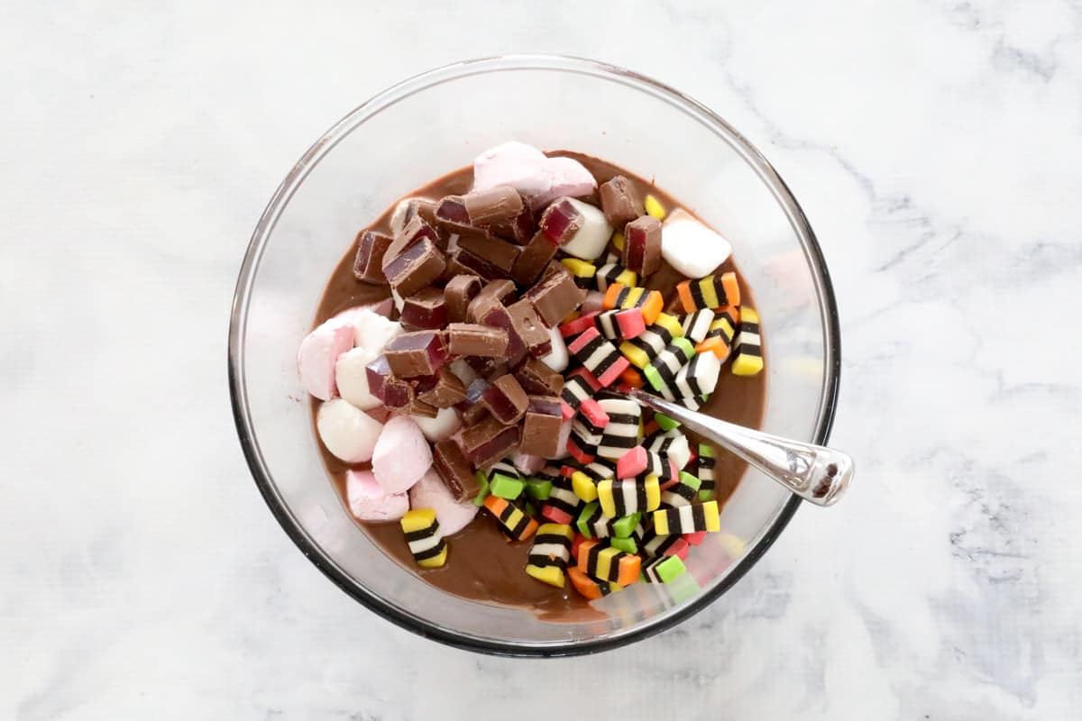 Licorice allsorts, marshmallows, and pieces of chocolate covered Turkish delight being stirred into melted milk chocolate