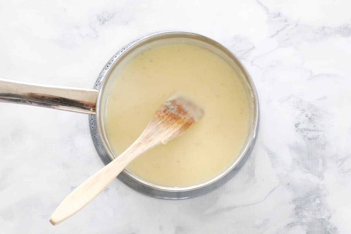 White cheese sauce in a saucepan, with a wooden spoon.