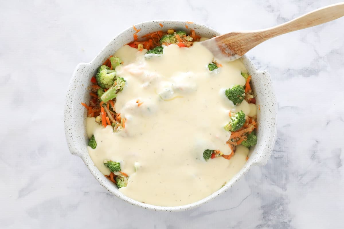 Cheese sauce poured over vegetables in a baking dish.