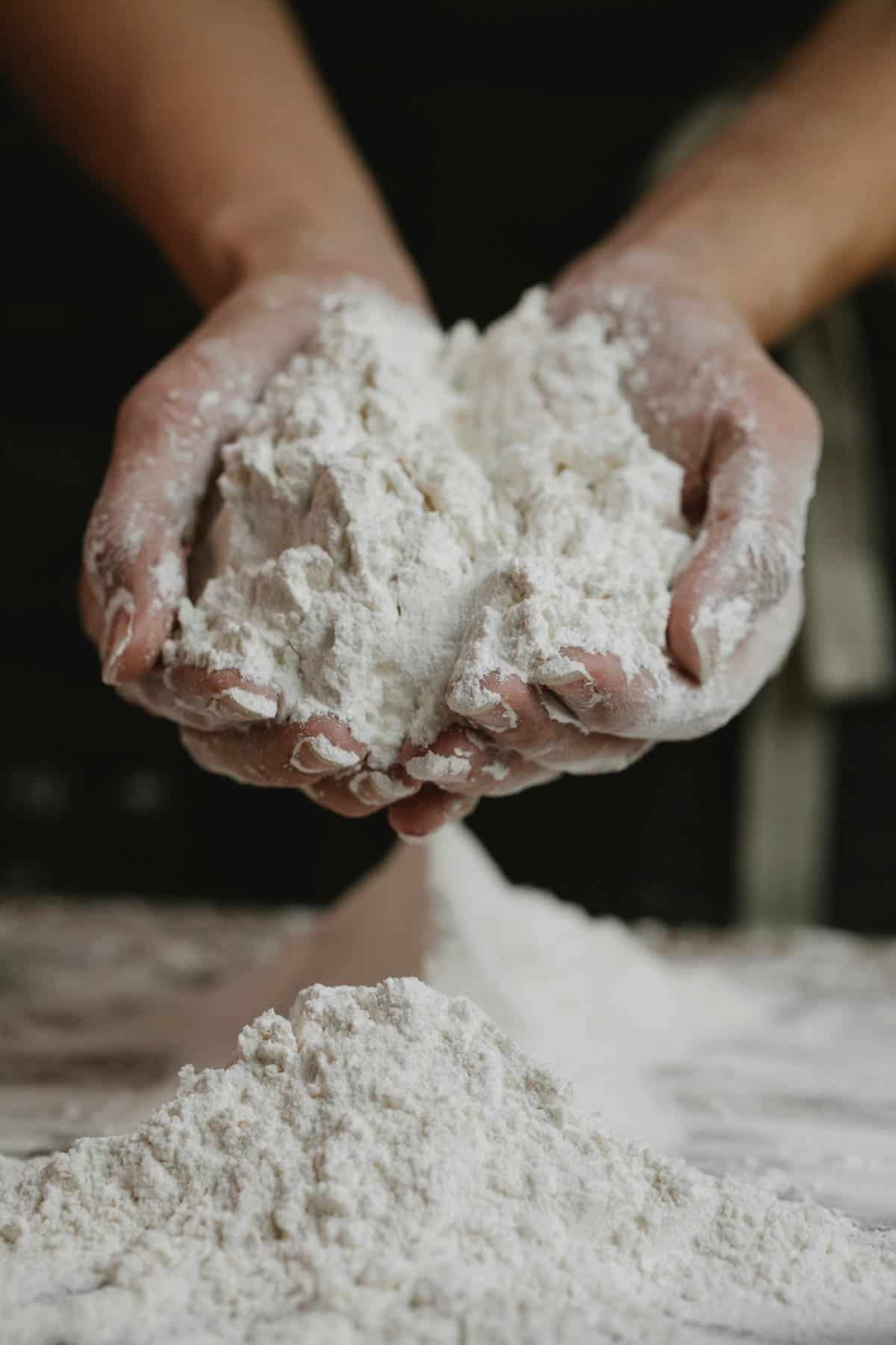 Two hands holding self raising flour over a bench.