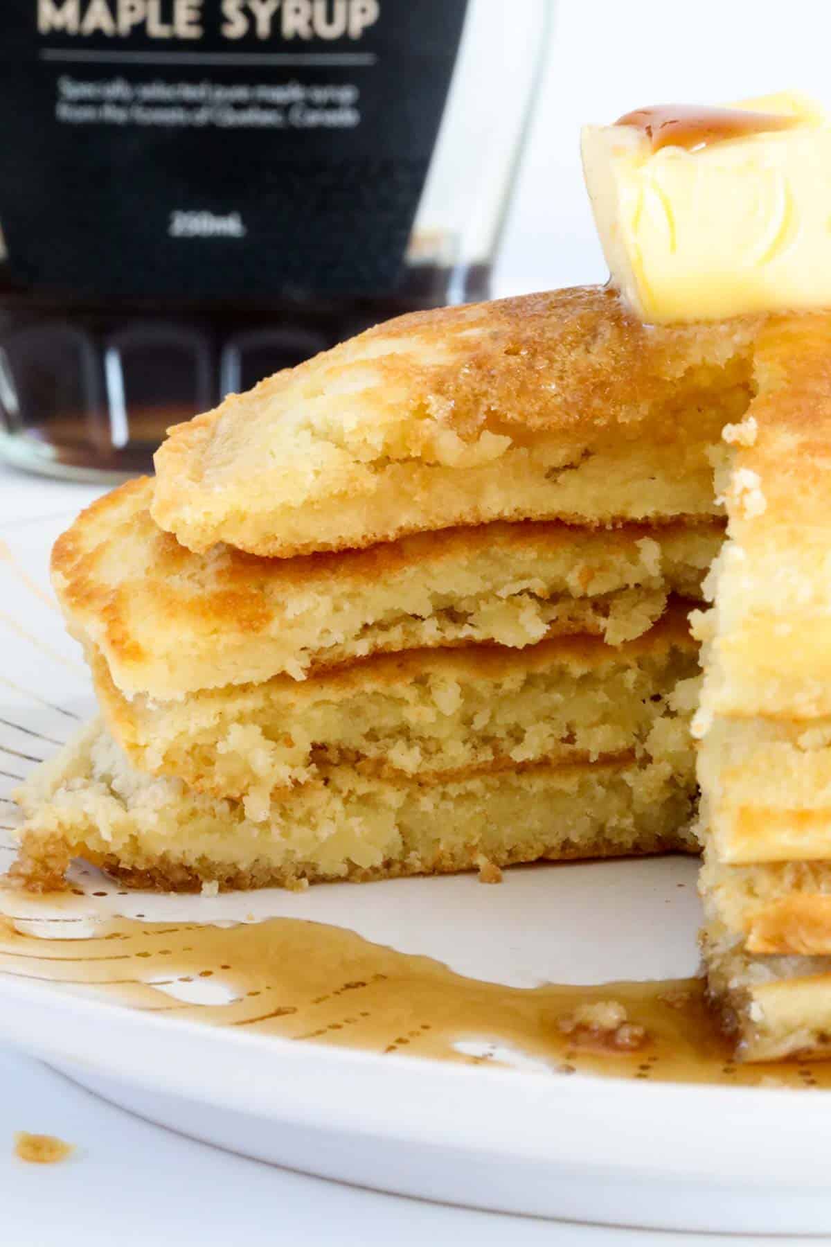 A stack of half-eaten fluffy pancakes with maple syrup and butter.