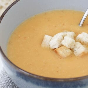 a bowl of soup with croutons and bread on the side