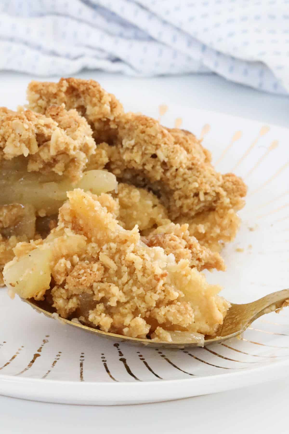 A gold patterned white plate with a spoonful of Apple Crumble resting on it