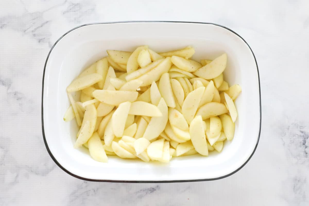 An enamel baking dish with thinly sliced stewed apples laid in the base.