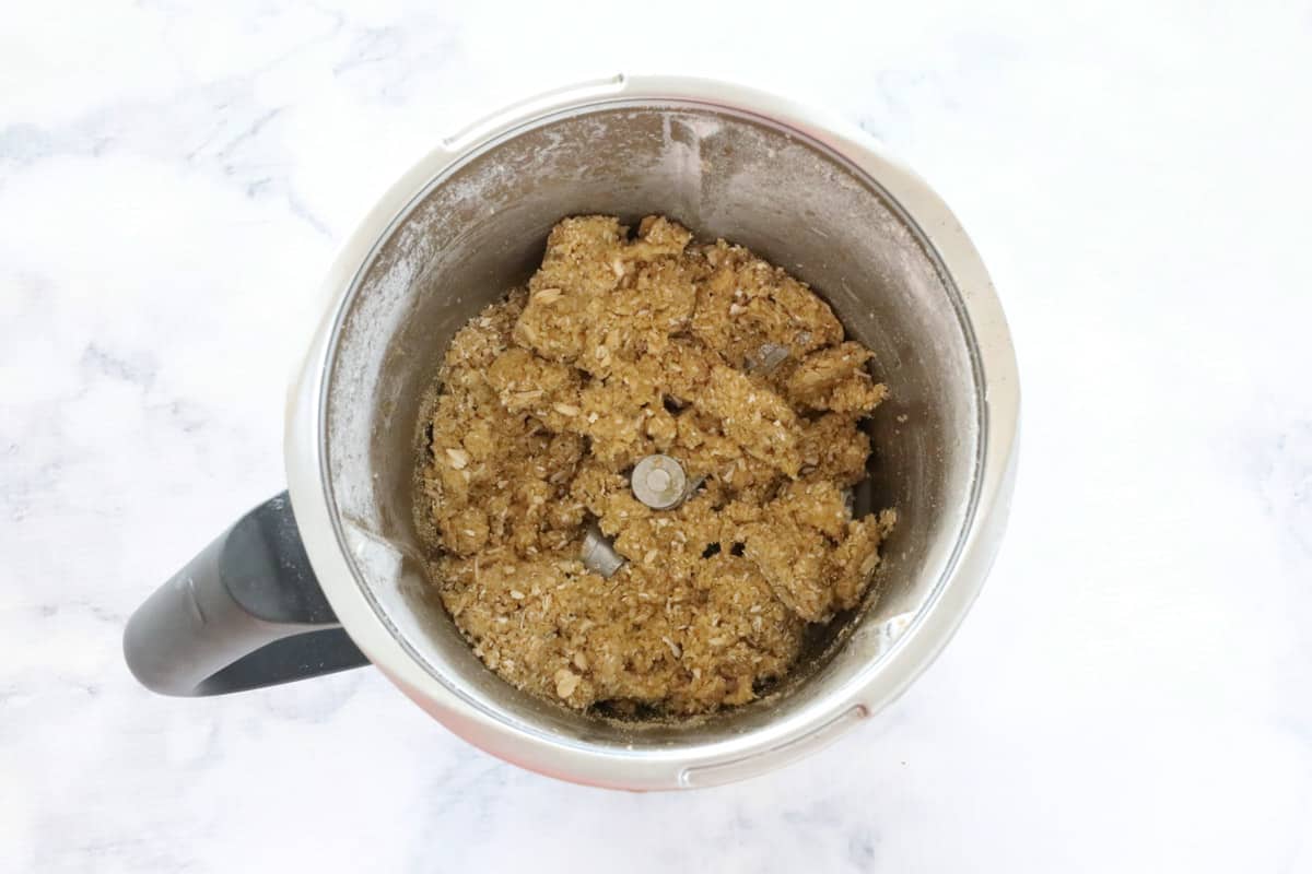 A brown coarse dough in a Thermomix mixing bowl on a marble counter