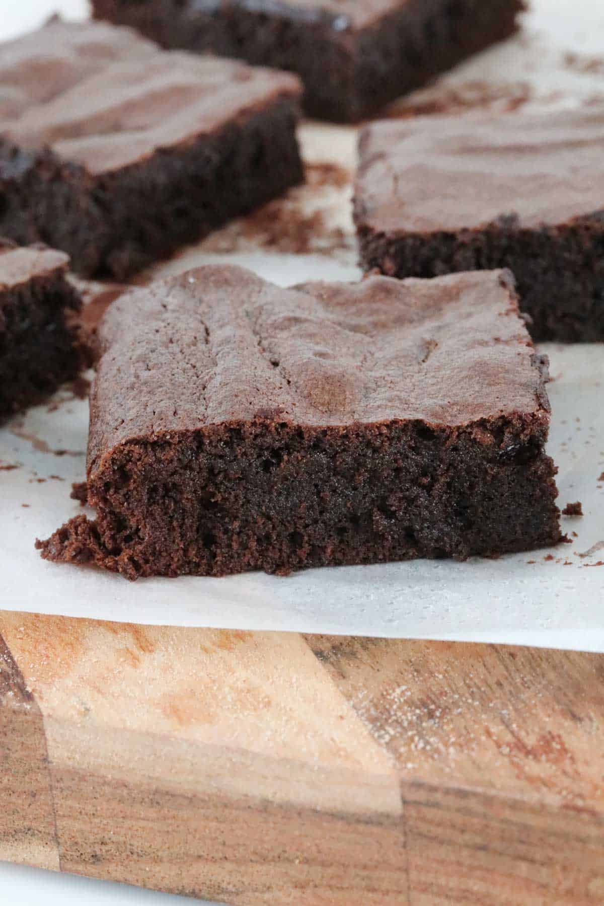 A rich square of chocolate brownie with a crusty top, resting on a wooden board.