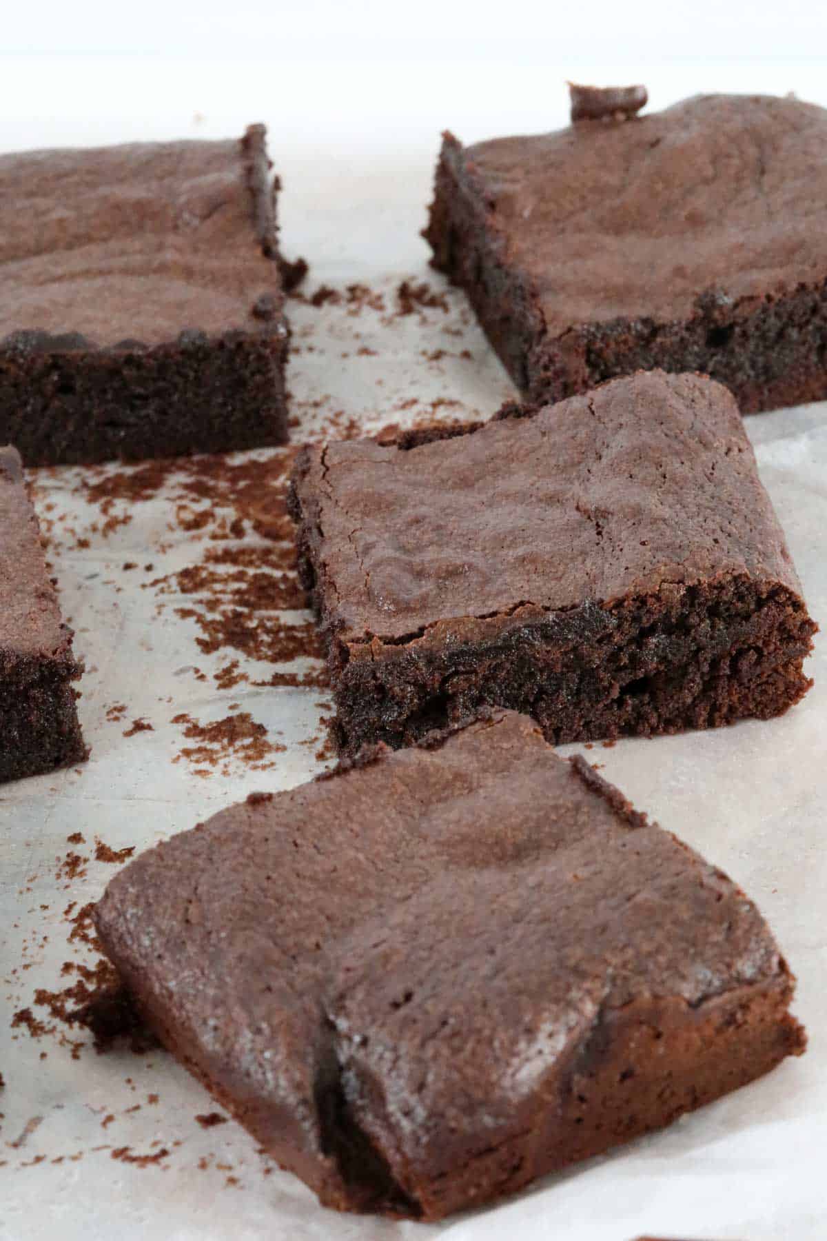 Crusty tops on dense fudgy brownies resting on baking paper.