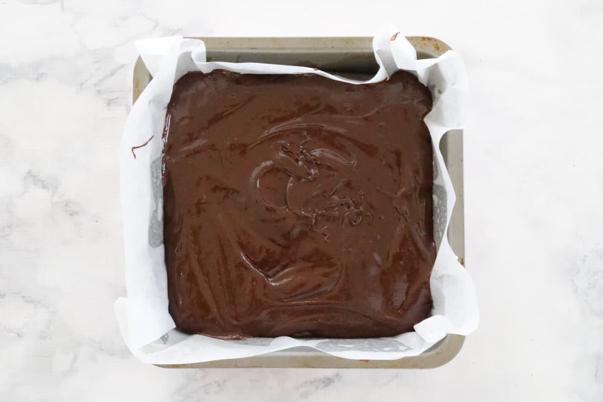 Brownie batter in a square paper lined baking tin.