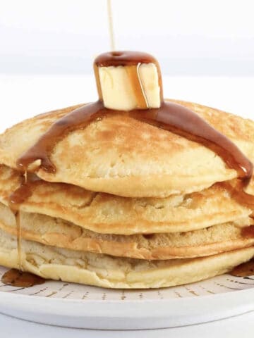 Maple syrup being poured over a stack of pancakes.
