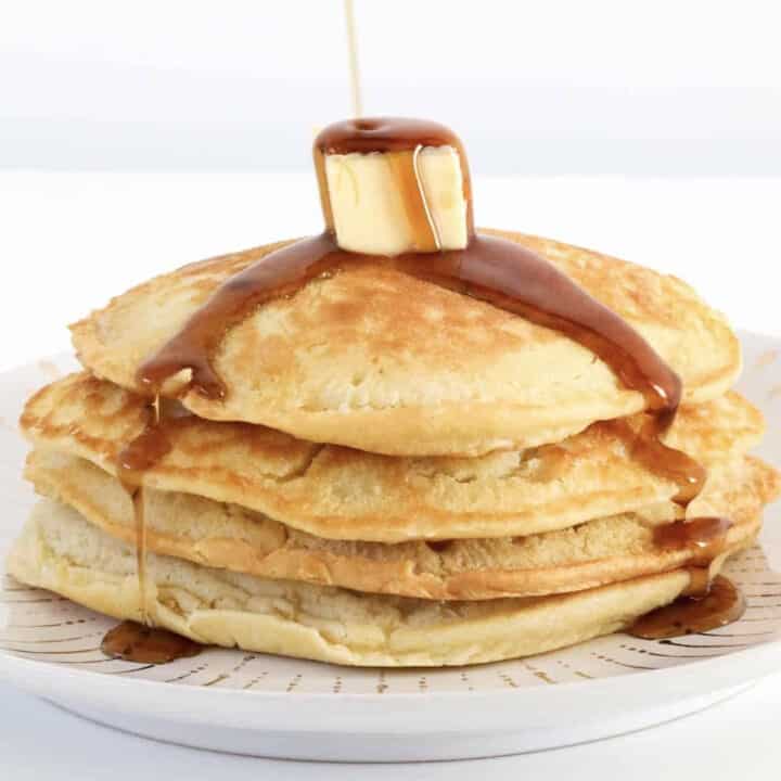 Maple syrup being poured over a stack of pancakes.