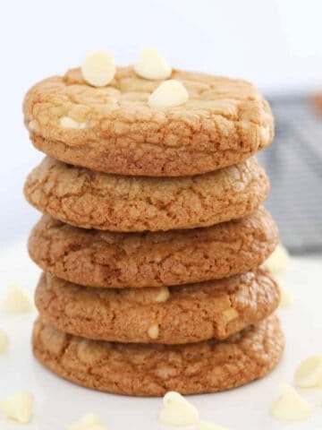 A stack of white chocolate chip cookies on a white cake stand