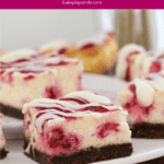 Squares of a cheesecake slice with raspberry swirls throughour and a chocolate base, served on a plate.