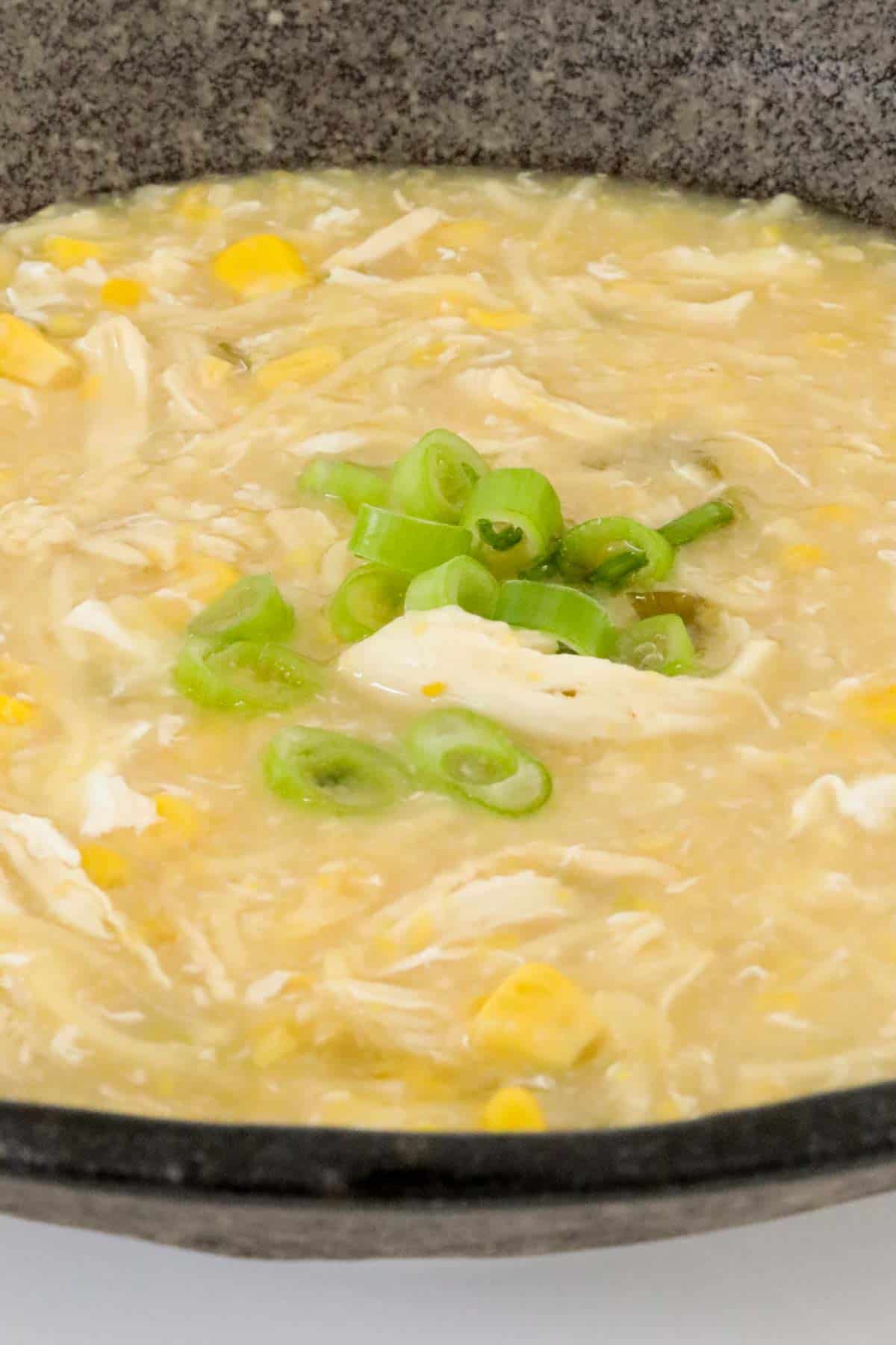 A close up of chicken, corn and noodle soup with spring onions sprinkled over the top.