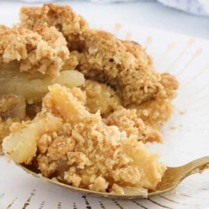 A white plate with a gold pattern with a spoonful of Apple Crumble resting on it