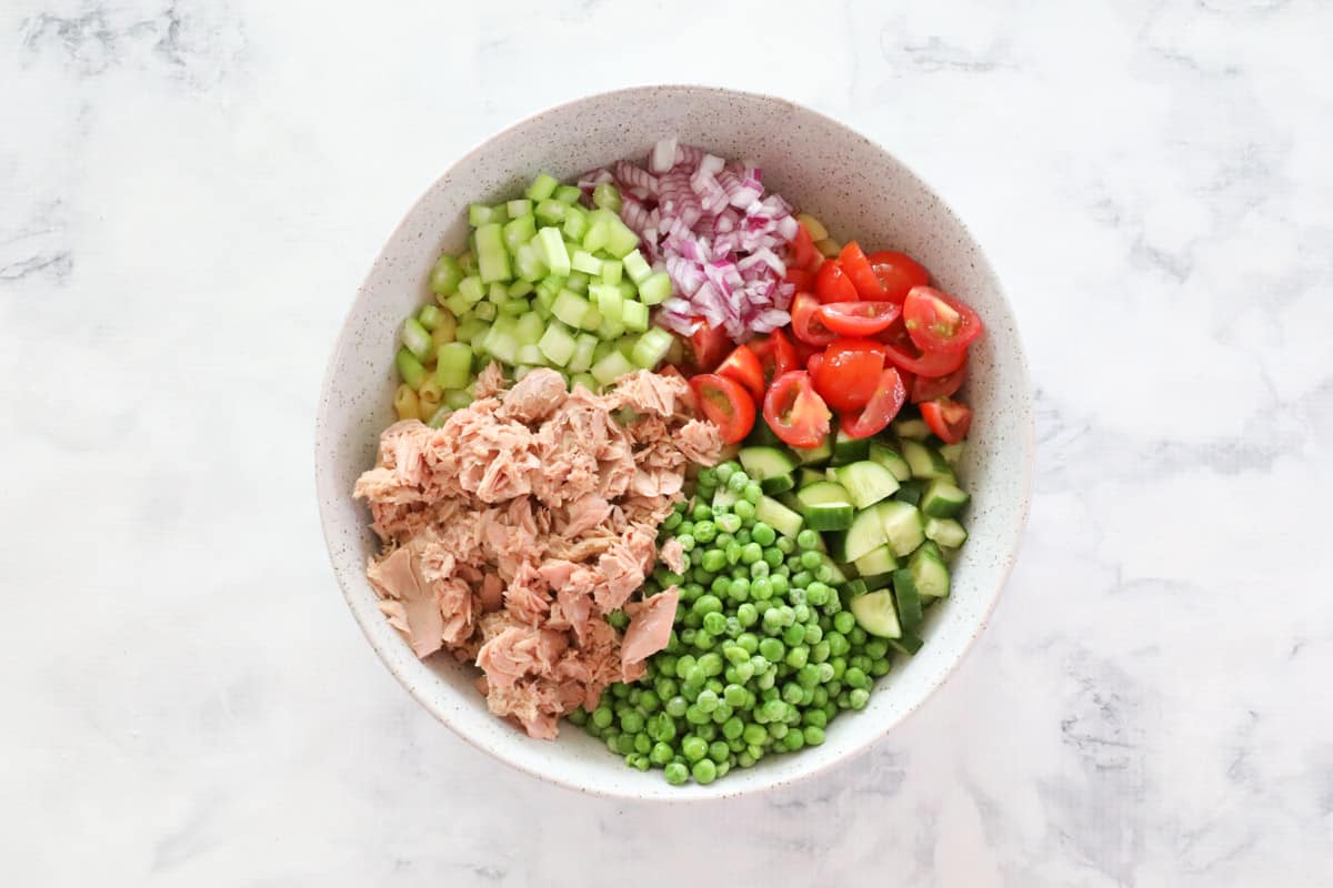 Chopped vegetables and tuna over macaroni in a white bowl