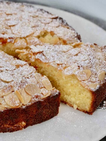 A slice of moist almond and coconut cake with flaked almonds and icing sugar on top.