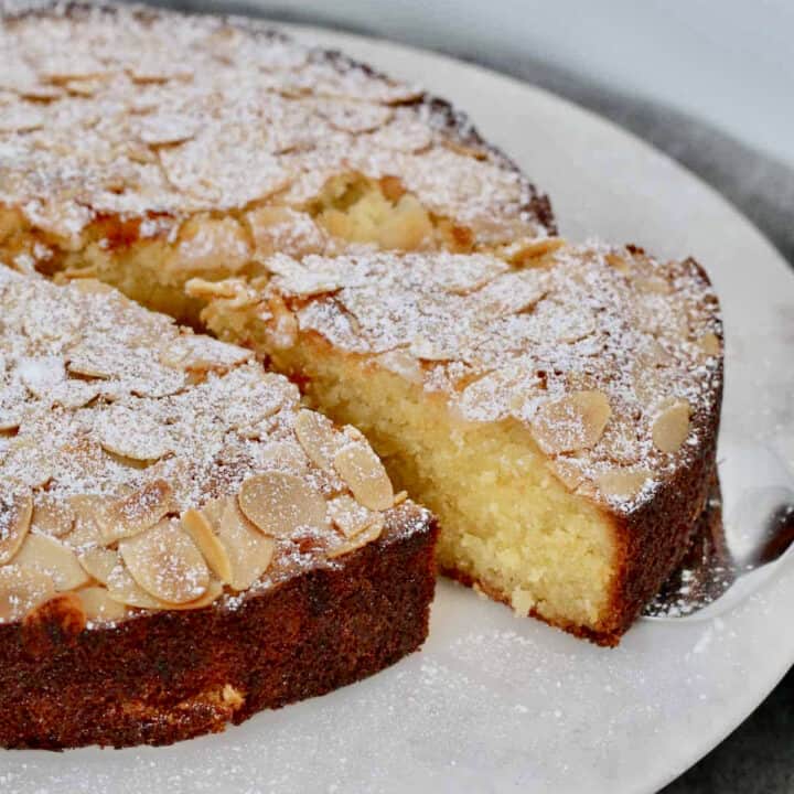 A slice of moist almond and coconut cake with flaked almonds and icing sugar on top.