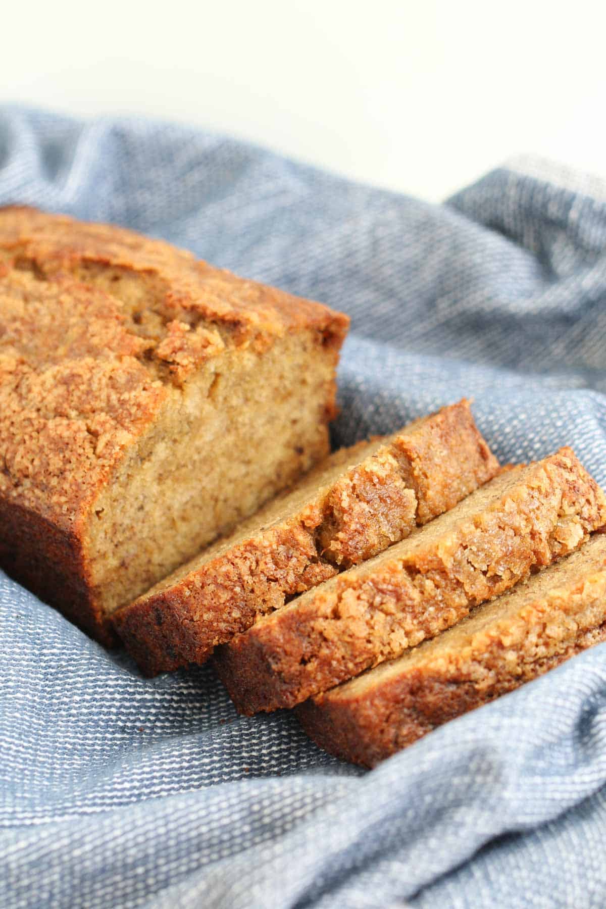 Slices of banana bread with a crunchy sugar topping on a blue tea towel.
