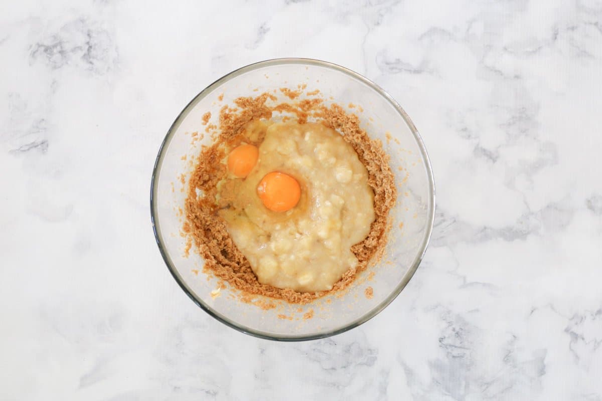 Mashed banana and eggs on top of creamed butter and sugar in a bowl.