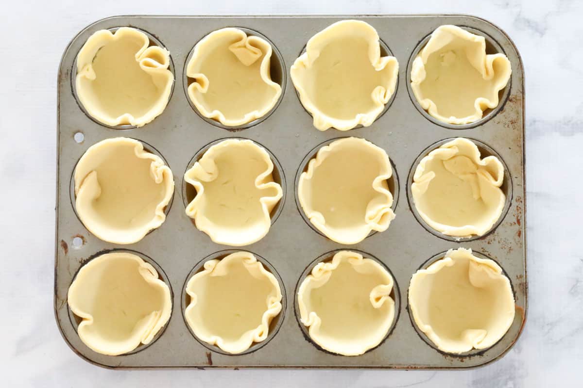 Shortcrust pastry rounds pressed into a muffin tray